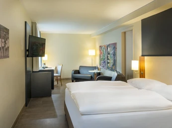 Business Zimmer Modernes Hotelzimmer mit Doppelbett, Sitzbereich, Flachbild-TV und stilvoller Wanddekoration.</p>Modern hotel room with double bed, seating area, flat-screen TV and stylish wall decorations.</p> <p