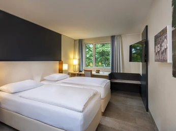 Essential Twin Zimmer Zweibettzimmer mit moderner Einrichtung, großem Fenster und Schreibtisch, ideal für Komfort und Ruhe.Double room with modern furnishings, large window and desk, ideal for comfort and rest.