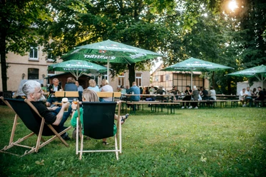 Biergarten Menschen auf Stühlen und Bänken mit Getränken.