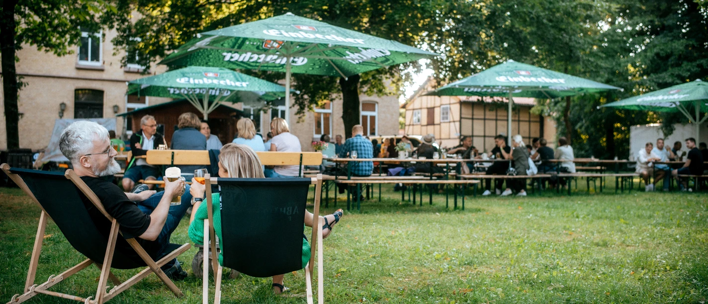 Biergarten Menschen auf Stühlen und Bänken mit Getränken.