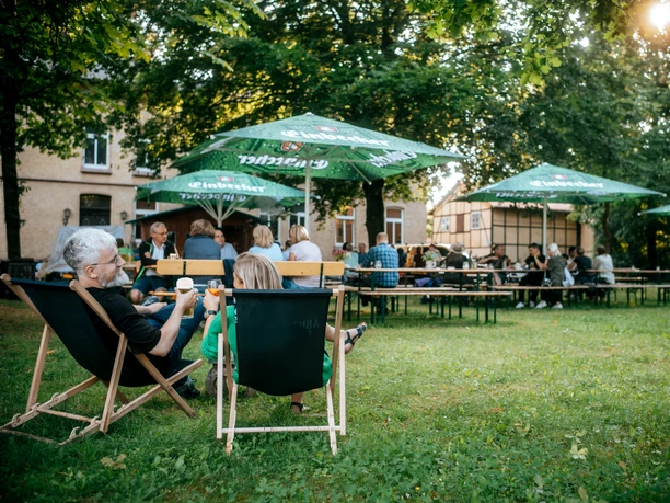 Biergarten Menschen auf Stühlen und Bänken mit Getränken.