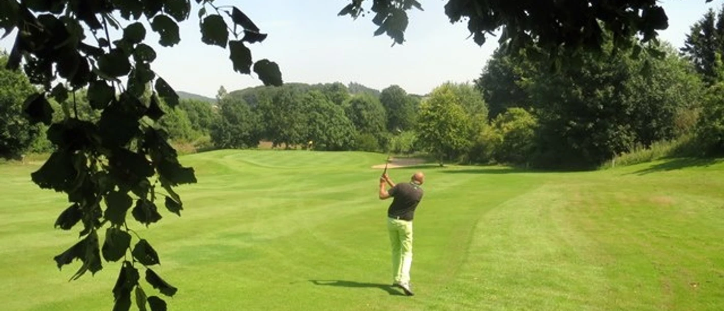 Golfer beim Abschlag auf grünem Fairway des Golfclubs Brilon, umrahmt von Bäumen