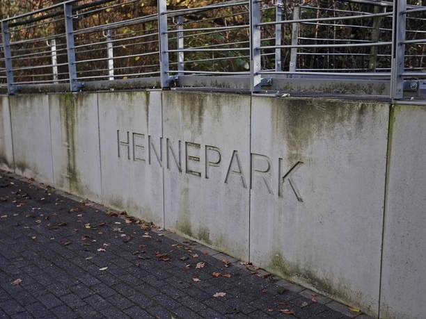 Betonmauer mit dem Schriftzug „HENNEPARK“ und Metallgeländer am Weg.