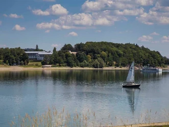 Segelboot auf dem Hennesee vor bewaldetem Ufer bei Meschede unter wolkigem Himmel