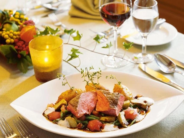 Angerichtetes Fleischgericht mit Gemüse, Kartoffeln, Kerze und Weingläsern im Restaurant