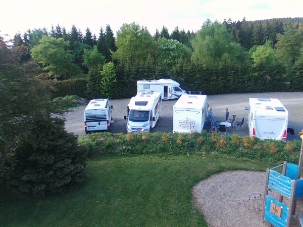 Wohnmobile auf einem Stellplatz am Waldrand, mit Grünfläche und Spielplatz im Vordergrund