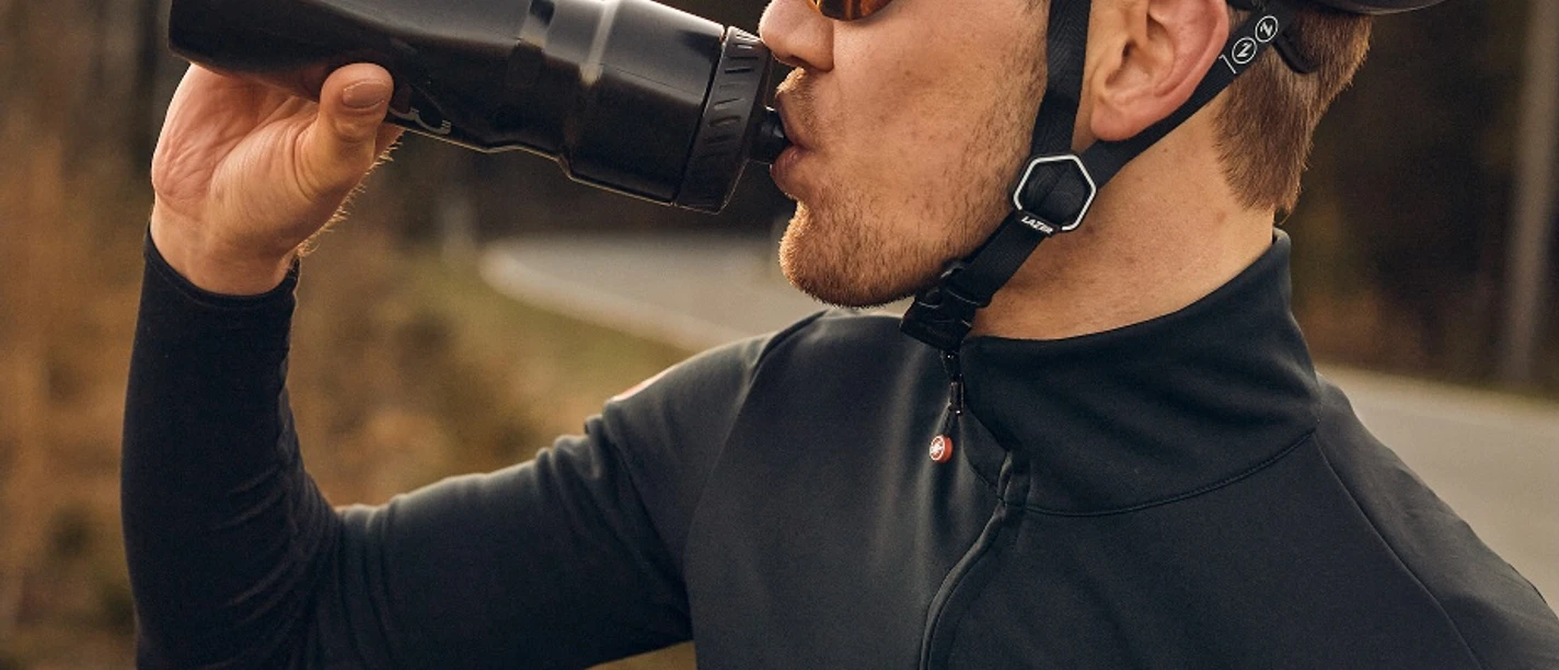 Rennrad im Sauerland Rennradfahrer mit Helm trinkt bei Sonnenuntergang am Waldrand aus einer Flasche