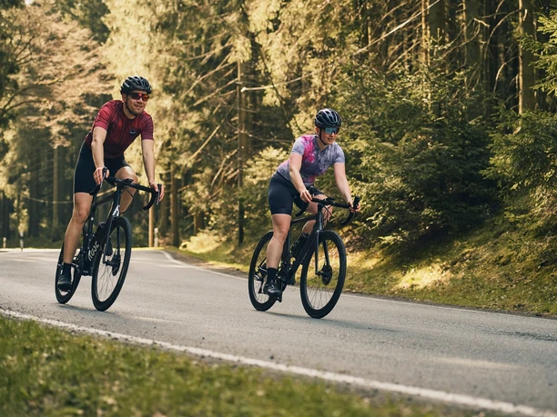 Zwei Rennradfahrer auf einer sonnigen Waldstraße im Sauerland