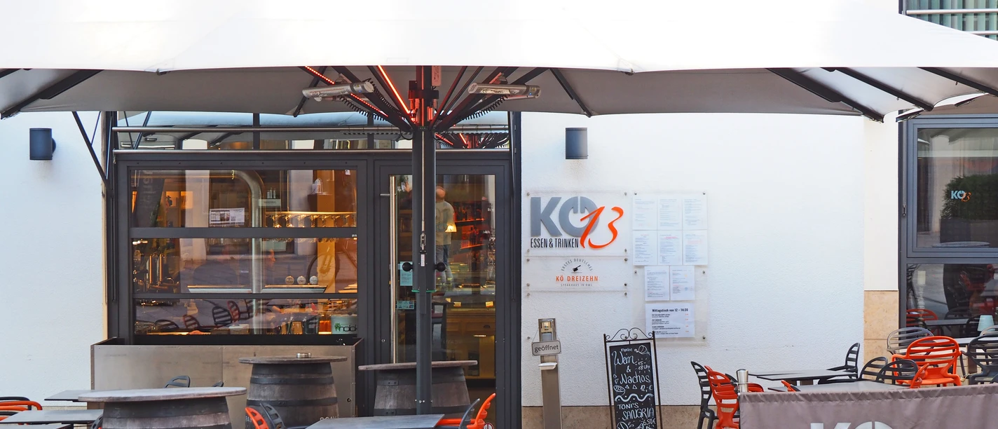 Restaurant Kö13 mit Außenterrasse, modernen orange-grauen Möbeln und großen Sonnenschirm.