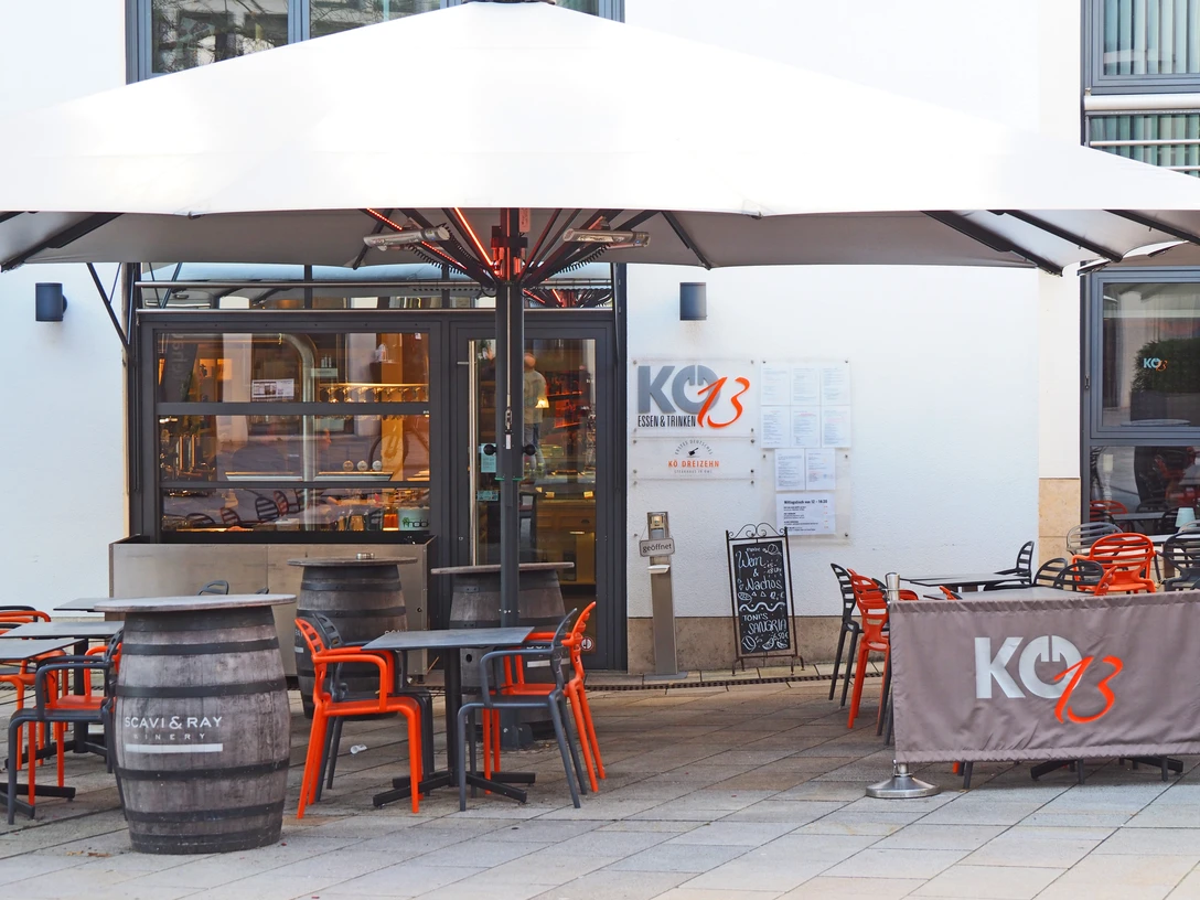 Kö13 Restaurant Kö13 mit Außenterrasse, modernen orange-grauen Möbeln und großen Sonnenschirm.