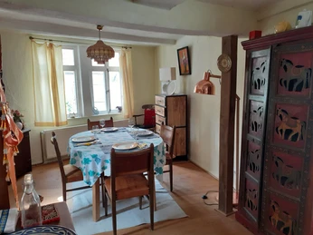 Wohnung_Innenbereich2.jpg Essbereich mit gedecktem Tisch, Holzmöbeln, farbenfroher Tischdecke und reich verziertem Schrank.