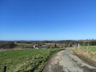 Weg hinunter nach Beckinghausen Asphaltierter Weg. Rechts und links abgezäunte Wiesen. Im Hintergrund das Dorf Beckinghausen. Am Horizont Wald und tiefblauer Himmel.