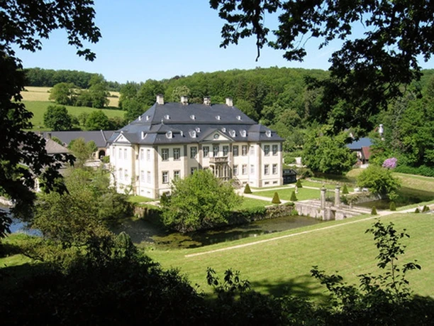 Schloss Körtlinghausen mit Parkanlage, Teich und bewaldeten Hügeln im Hintergrund