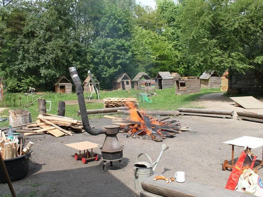Abenteuerspielplatz Eschborn Bauphase von kleinen Holzhütten. Davor brennt ein Lagerfeuer