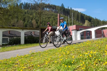 DampfLandLeute Museum Eslohe Zwei Radfahrer vor dem DampfLandLeute Museum Eslohe, Wiese und Wald im Hintergrund
