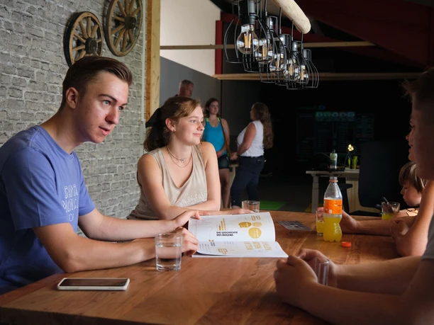 Gemütlich sitzen Eine Gruppe junger Menschen sitzt an einem Tisch in einem Restaurant. Im Hintergrund steht eine weitere Gruppe