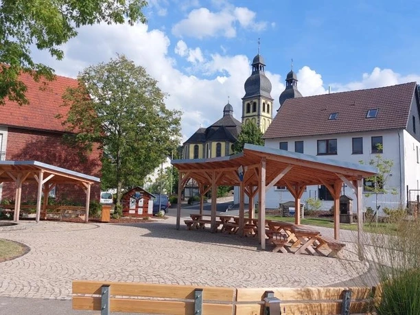 Dorfplatz in Padberg mit Holzdächern, Bänken und Kirche vor bewaldetem Hang
