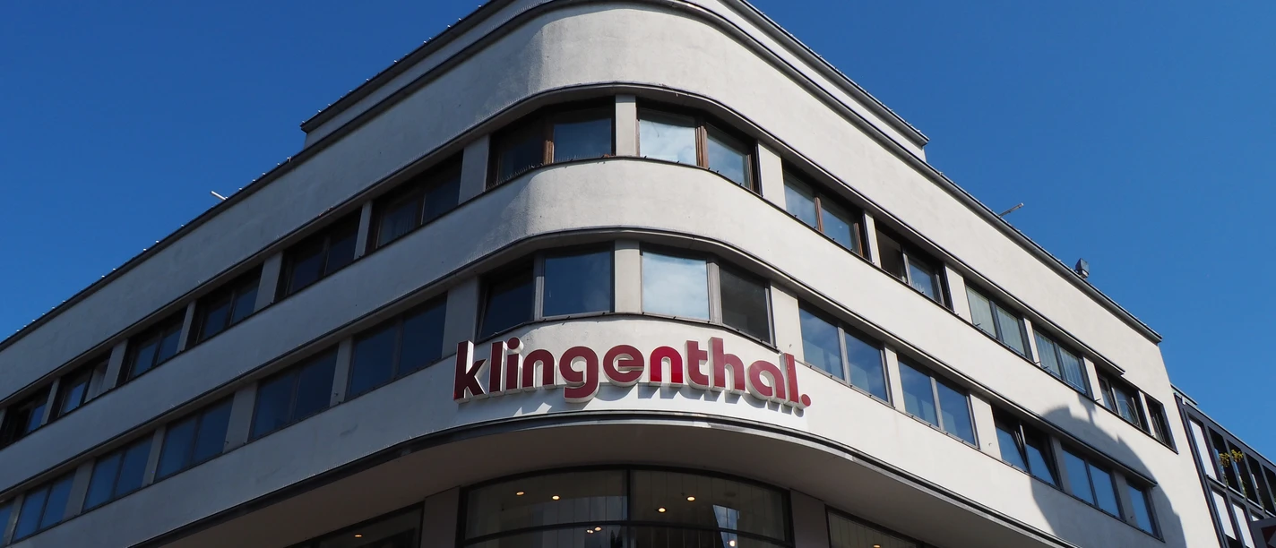 Fassade des Kaufhauses Klingenthal Kaufhaus Klingenthal mit moderner Fassade, großen Glasfronten und rotem Schriftzug bei klarem Himmel.
