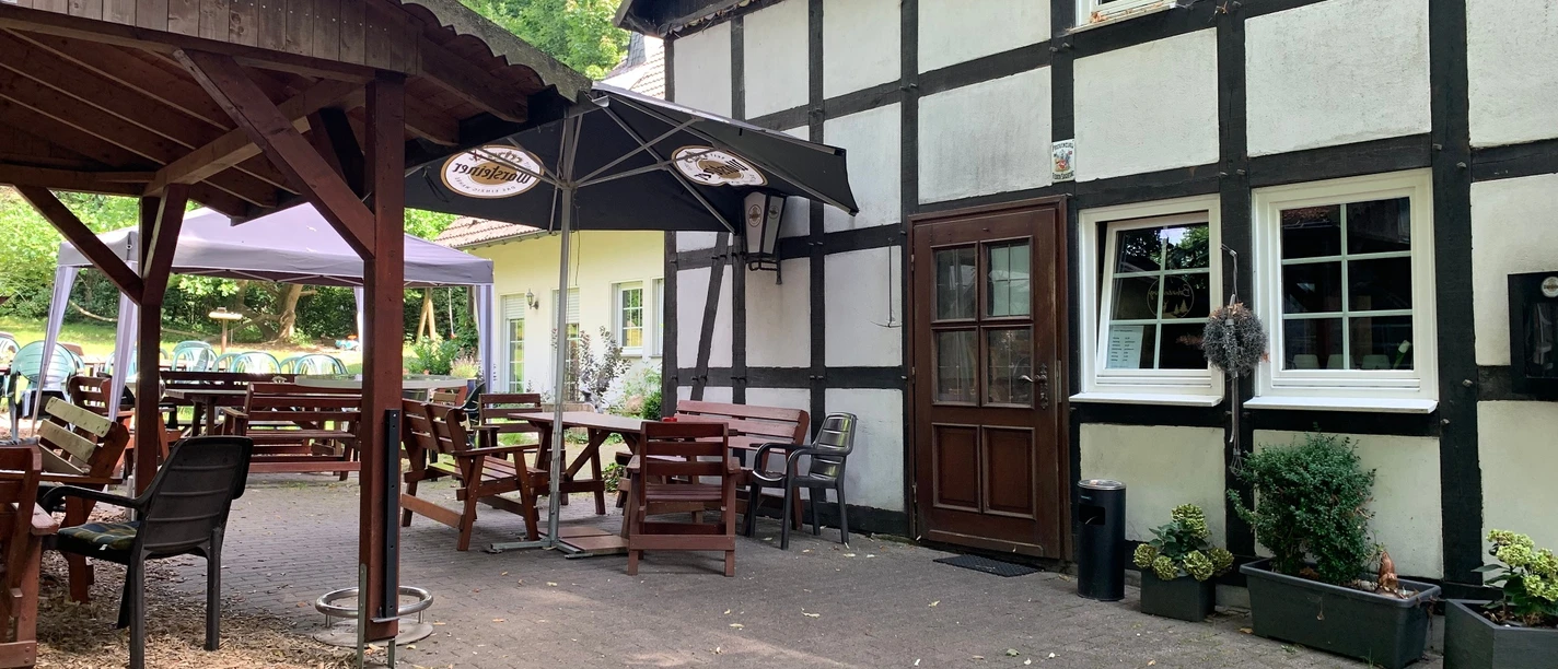 Fachwerkfassade des Gasthofs Zur Bohnenburg mit Biergarten und Sonnenschirmen in Suttrop