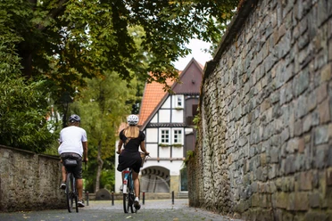 Zwei Radfahrende in Soests Altstadtgasse vor Fachwerkhaus und historischer Stadtmauer
