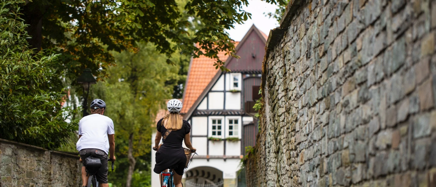 Zwei Radfahrende in Soests Altstadtgasse vor Fachwerkhaus und historischer Stadtmauer