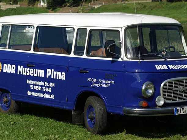 Barkas im DDR-Museum Pirna Blauer Oldtimer-Bus mit weißem Dach, beschriftet mit "DDR Museum Pirna", steht auf einer grünen Wiese.