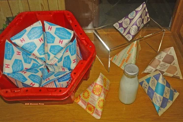 Rode krat met blauwe en witte gecondenseerde melkpakken, daarnaast verschillende gekleurde melkpakken en een glazen fles op een houten tafel.