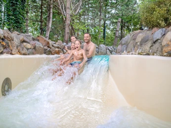 Center_Parcs_2.jpg Das Bild zeigt eine fröhliche Familie auf einer Wasserrutsche, umgeben von Bäumen, im Center Parcs Bispingen.