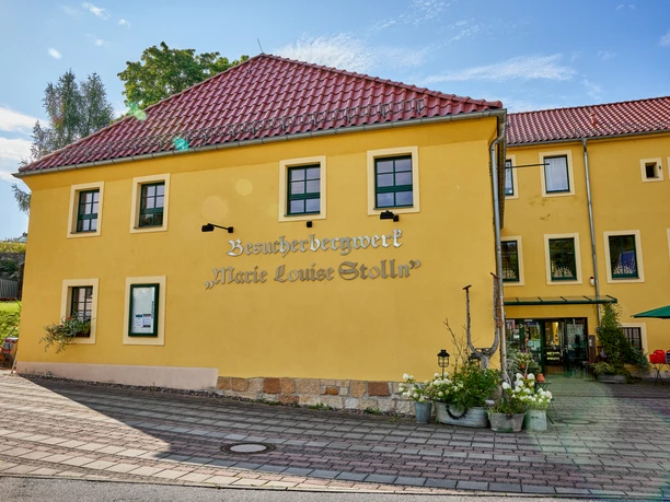 Yellow building in traditional style with red tiled roof, surrounded by blooming flowers and sidewalk.