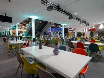 Tagungen_4.jpg Großes, modernes Café mit bunten Stühlen, weißen Tischen und farbenfroher Dekoration im Innenbereich.Large, modern café with colorful chairs, white tables and colorful interior decoration.