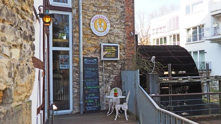 Mühlencafé Mühlencafé mit historischem Wasserrad und gemütlichem Außenbereich inmitten moderner Architektur.