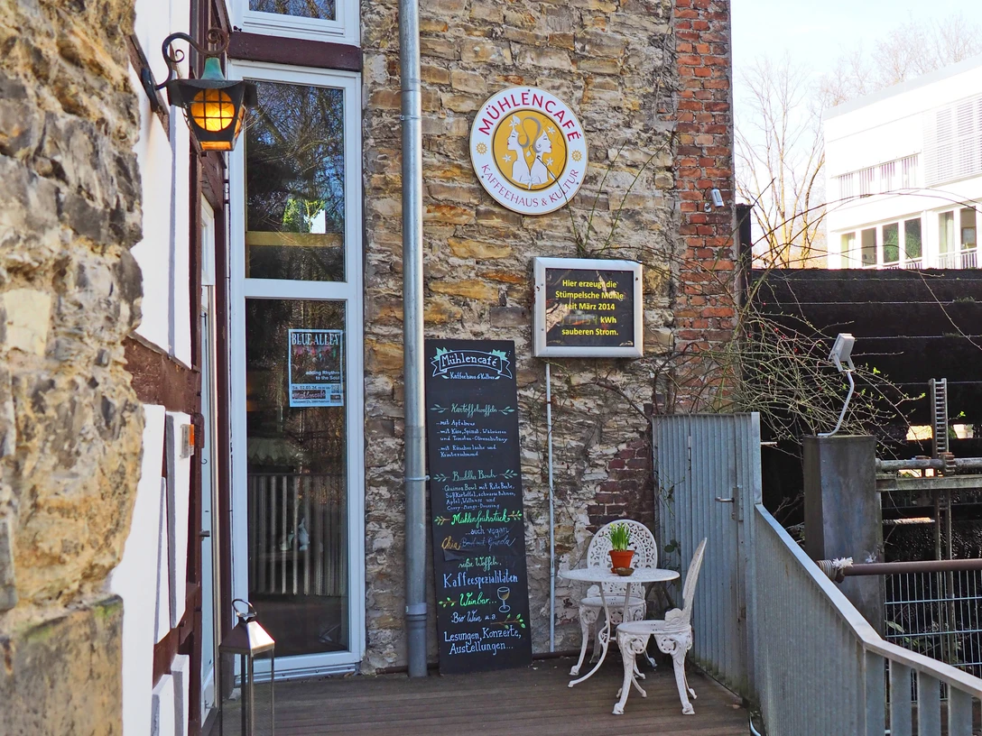 Mühlencafé Mühlencafé mit historischem Wasserrad und gemütlichem Außenbereich inmitten moderner Architektur.