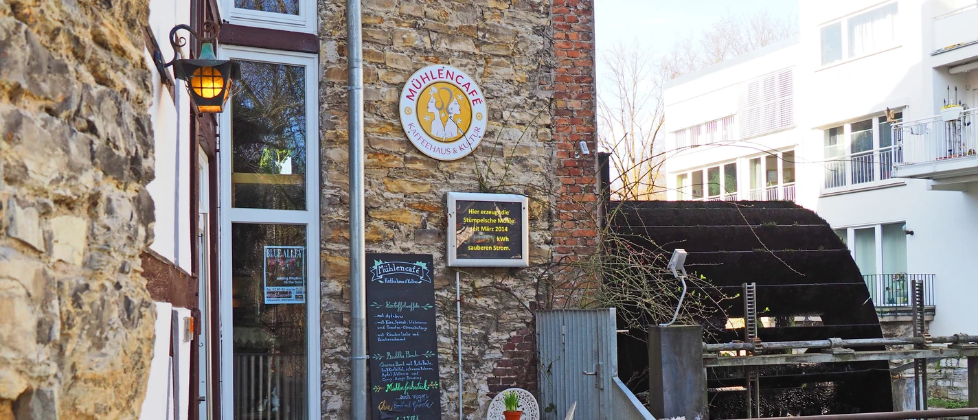Mühlencafé Mühlencafé mit historischem Wasserrad und gemütlichem Außenbereich inmitten moderner Architektur.