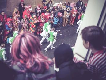 Karneval_3.jpg Karnevalsumzug: verkleidete Menschen stehen am Fenster und schauen auf weitere verkleidete Menschen auf der StraßeCarnival parade: people in costumes stand at the window and watch other people in costumes on the street