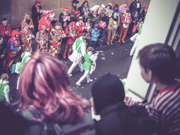 Karneval_3.jpg Karnevalsumzug: verkleidete Menschen stehen am Fenster und schauen auf weitere verkleidete Menschen auf der Straße