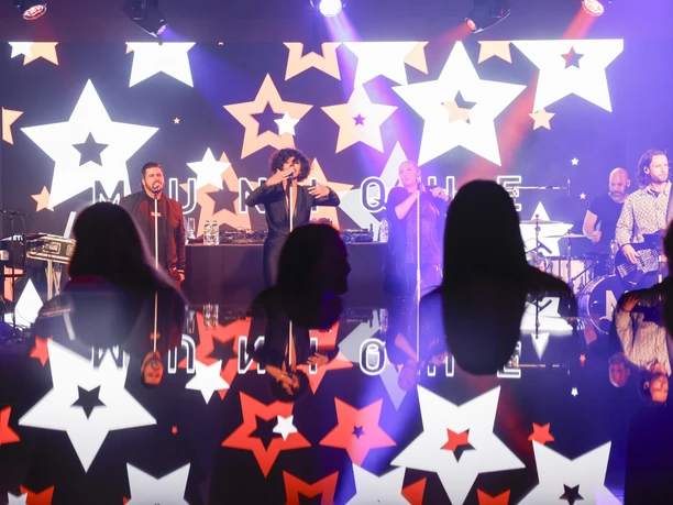 4_Events.jpg Live-Band spielt auf Bühne; Leuchtsterne im Hintergrund; Publikum in vorderem Bereich.