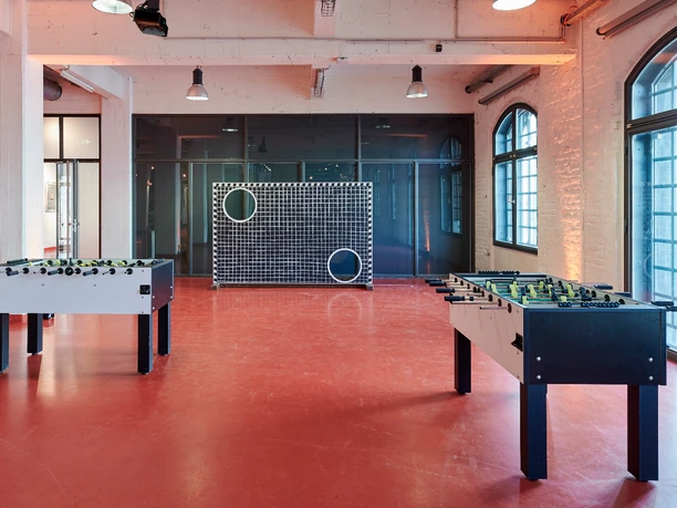 Activity Feld (18).jpg Zwei Tischkicker stehen in einem Raum mit roten Böden, Fenster und ein großformatiges Zielspielgerät.</p>