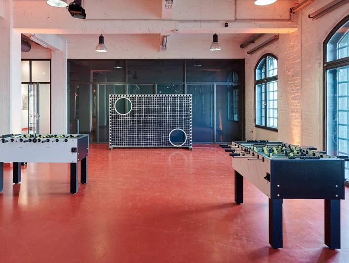 Activity Feld (18).jpg Zwei Tischkicker stehen in einem Raum mit roten Böden, Fenster und ein großformatiges Zielspielgerät.</p>Two table football tables stand in a room with red floors, windows and a large-format target game machine.