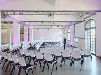Champions Hall Halbkreis.jpg Moderner Konferenzraum mit weißen Stühlen, großen Fenstern und stilvoller Beleuchtung.</p>Modern conference room with white chairs, large windows and stylish lighting.</p> <p