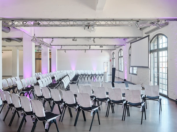 Champions Hall Halbkreis.jpg Moderner Konferenzraum mit weißen Stühlen, großen Fenstern und stilvoller Beleuchtung.</p>