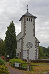 Turm der Kirche St. Maria in Helminghausen mit Kreuz und Rundfenster vor grauem Himmel