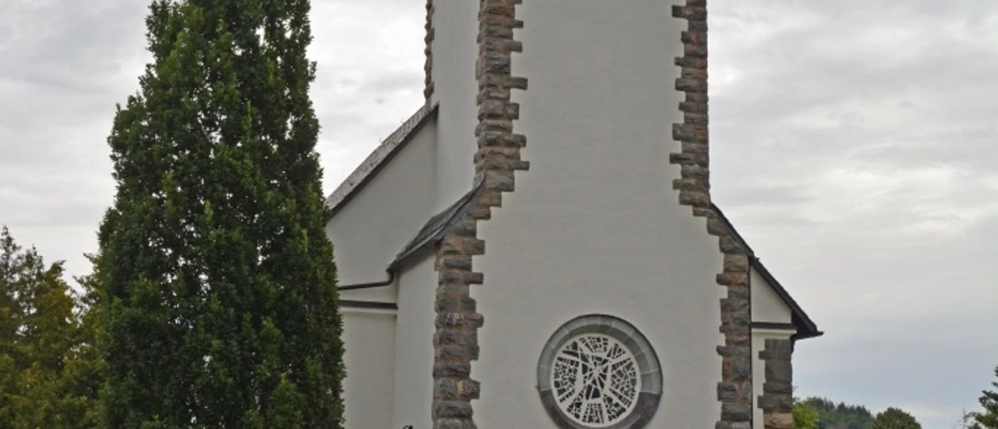 Turm der Kirche St. Maria in Helminghausen mit Kreuz und Rundfenster vor grauem Himmel
