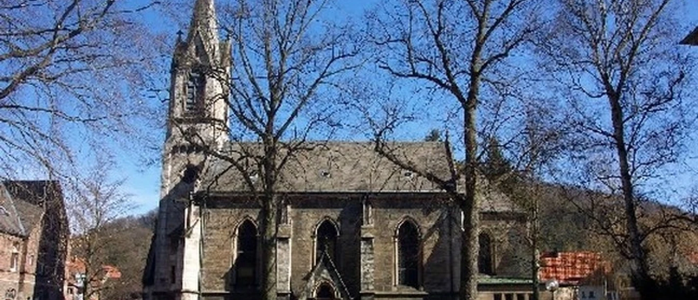 St. Johannes von Gott in Marsberg mit Turm, hohen Fenstern und Bäumen im Vordergrund