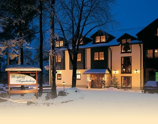 Berghotel Augustusberg Ein verschneites Berghotel mit beleuchteten Fenstern und Eingang, umgeben von schneebedeckten Bäumen.
