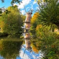 Stadt Petershagen_Lahde_Klostermühle_Herbst_Blick von Aue.jpg Eine historische Mühle mit drehenden Flügeln spiegelt sich in einem von buntem Herbstlaub umsäumten Fluss.