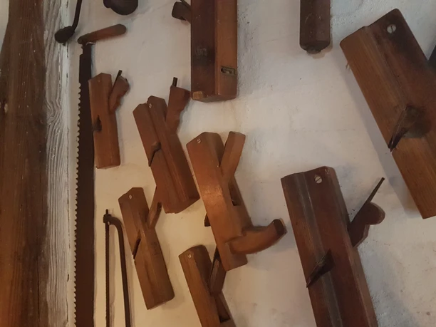 Mühlenmuseum©Dorothée Meyer (27).jpg Old wooden woodworking tools arranged on a white wall alongside a saw.