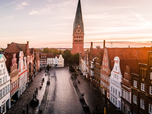 Platz am Sande in Lüneburg Platz Am Sande mit historischen Giebelhäusern und der St. Johanniskirche im Sonnenlicht.