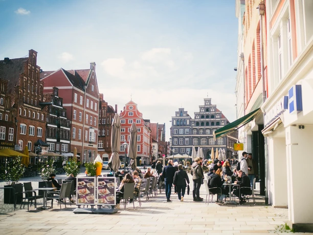 Platz Am Sande in Lüneburg mit historischen Backsteinhäusern, Cafés und Menschen im Sonnenschein.