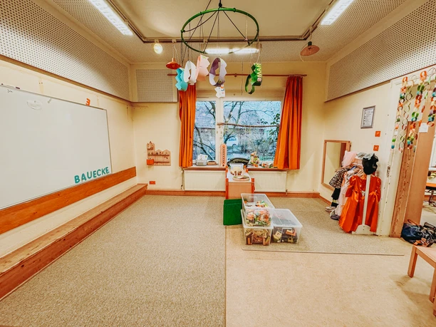 Heller Spielraum im Kindergarten mit Bauecke, Verkleidungskisten und buntem Fensterschmuck.