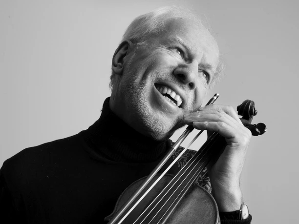 Gidon Kremer smiling with violin, black and white, humorous expression.
